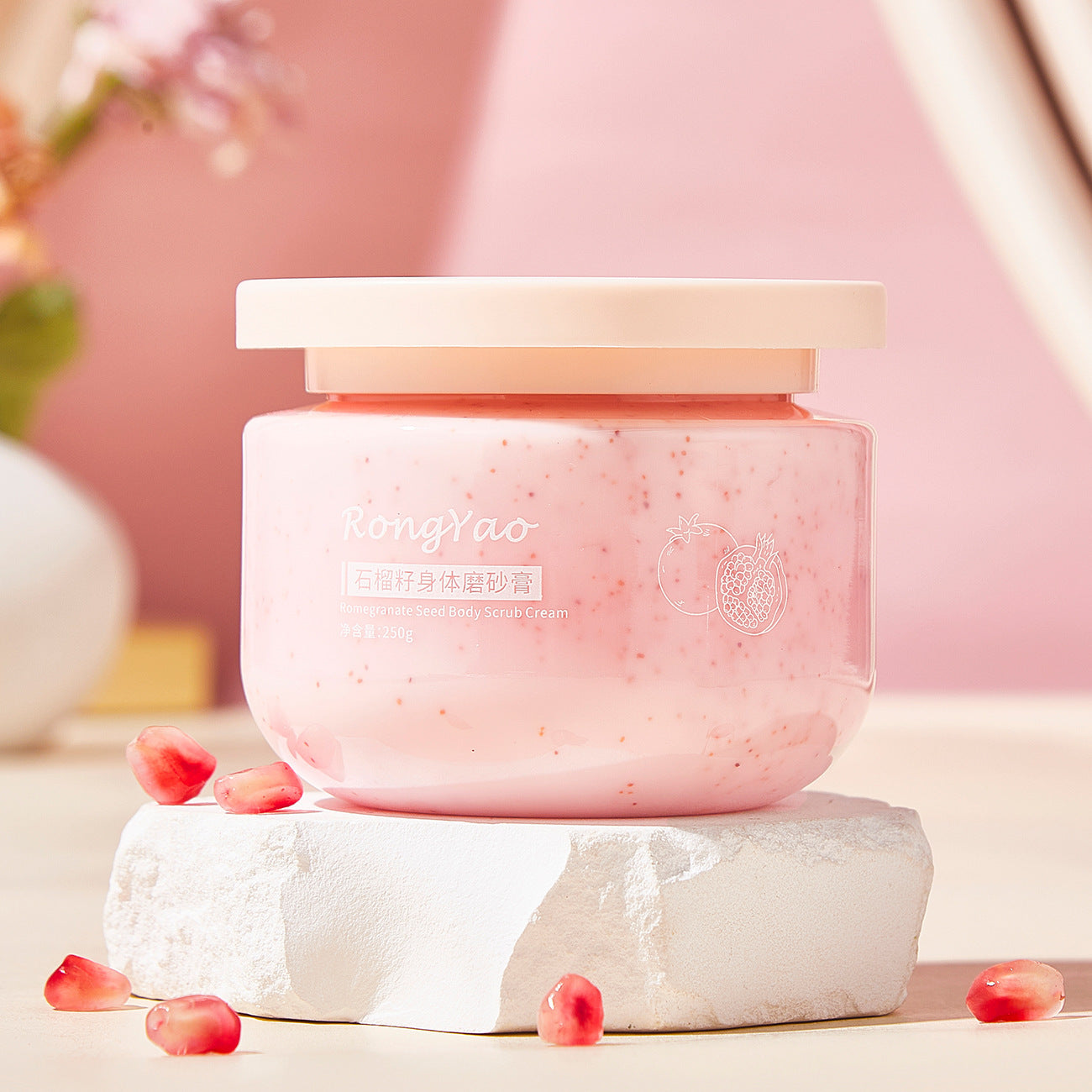 Avocado face scrub in a pink jar on a white stone, with pomegranate seeds around, showcasing natural skincare.